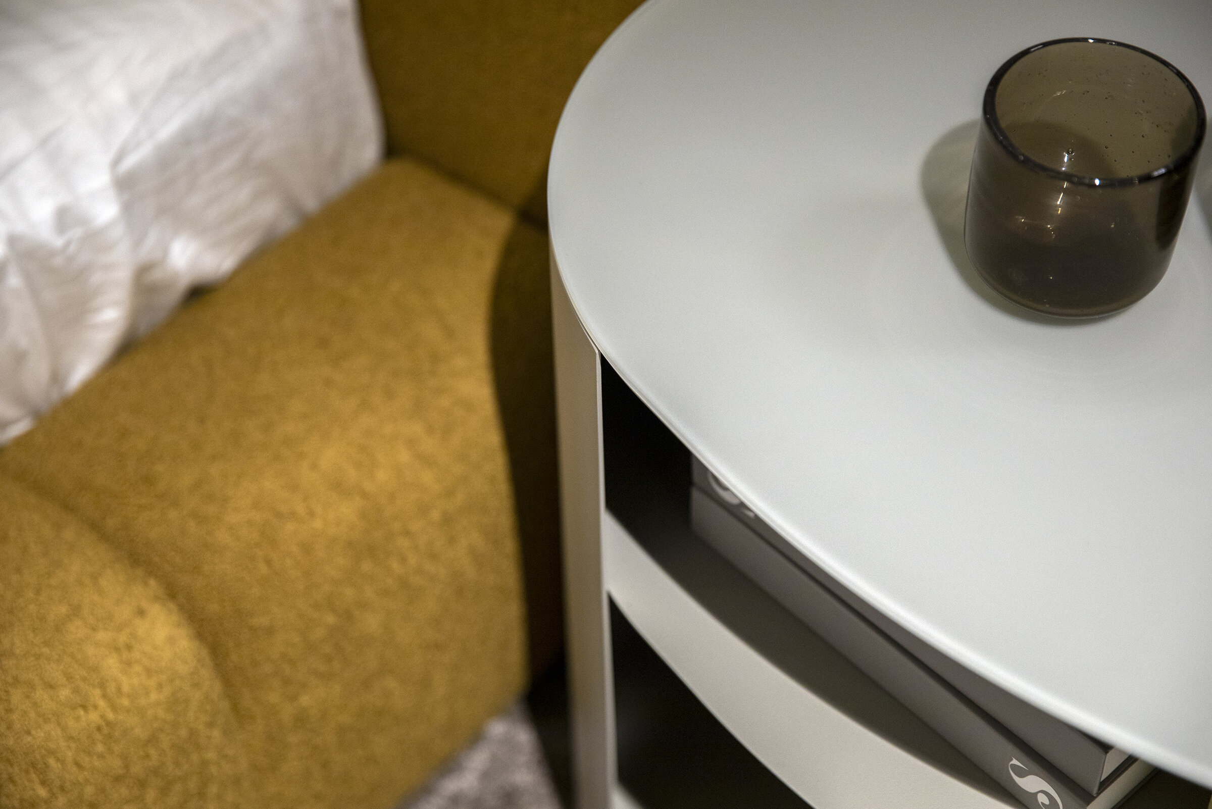 Sleek white round side table with a black glass vase, placed next to a mustard-yellow sofa, showcasing modern furniture design and interior decor for contemporary homes.
