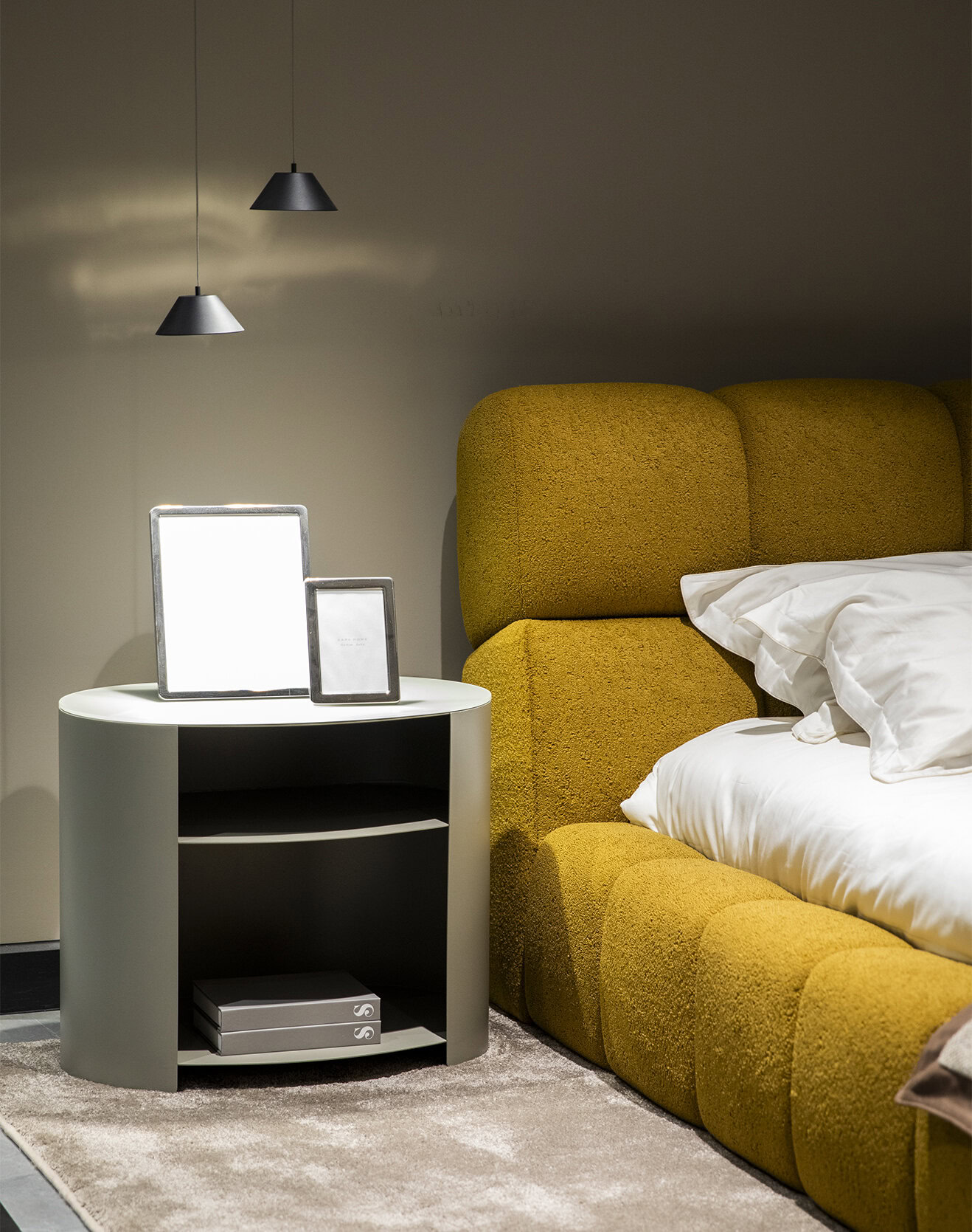 Luxurious yellow upholstered bed with modern design, complemented by a sleek white nightstand with framed photos, under stylish black pendant lights for a contemporary bedroom setting.