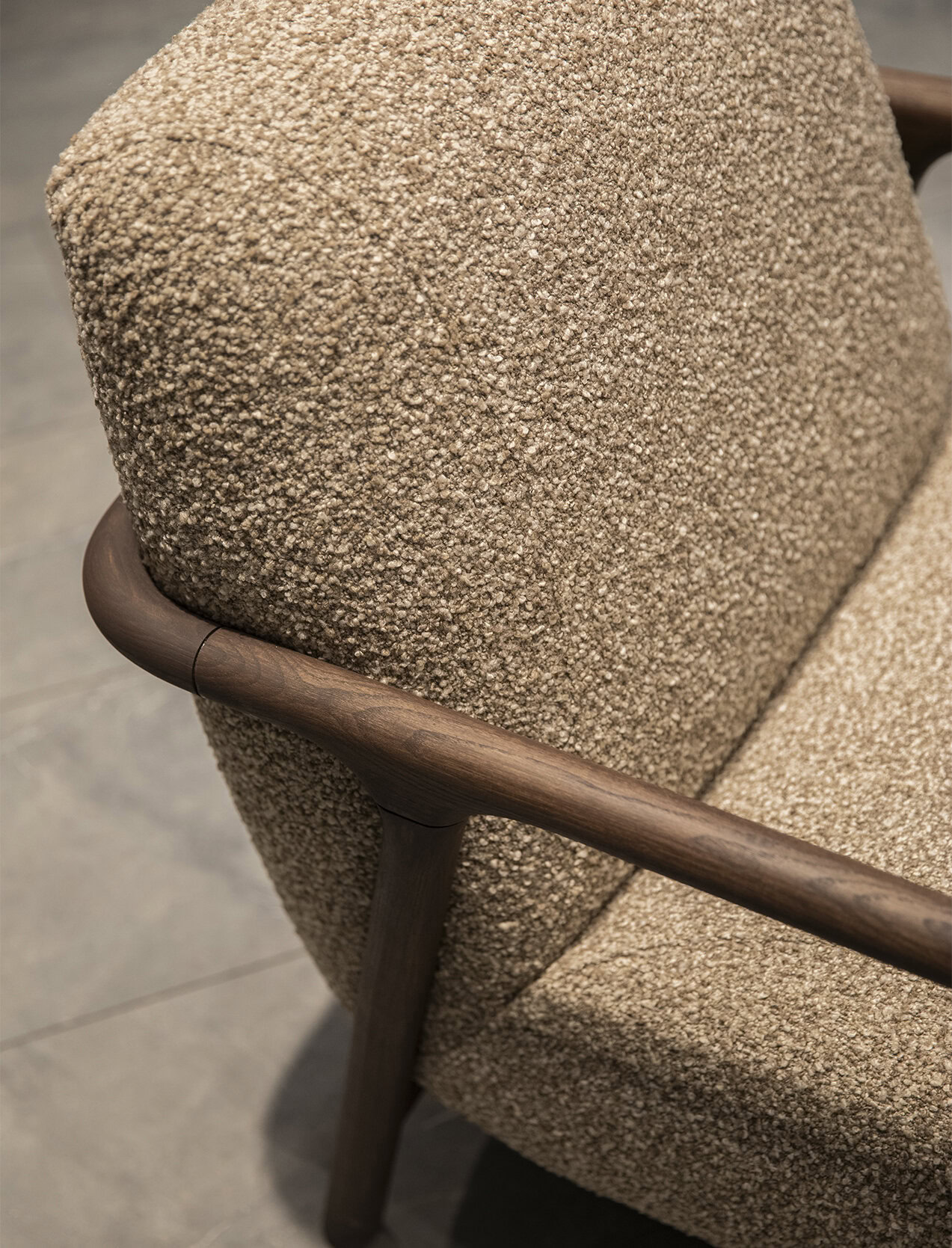 Soft textured beige fabric with smooth wooden armrest details, perfect for modern and contemporary living spaces. High-quality craftsmanship by Saloni Furniture offers comfort and durability.