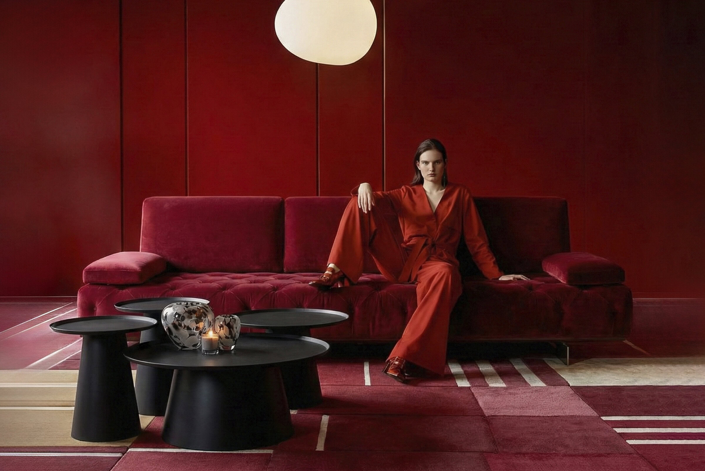 Elegant red velvet sofa from Saloni Furniture with a modern design, set against a matching red wall, complemented by black coffee tables and decorative vases.
