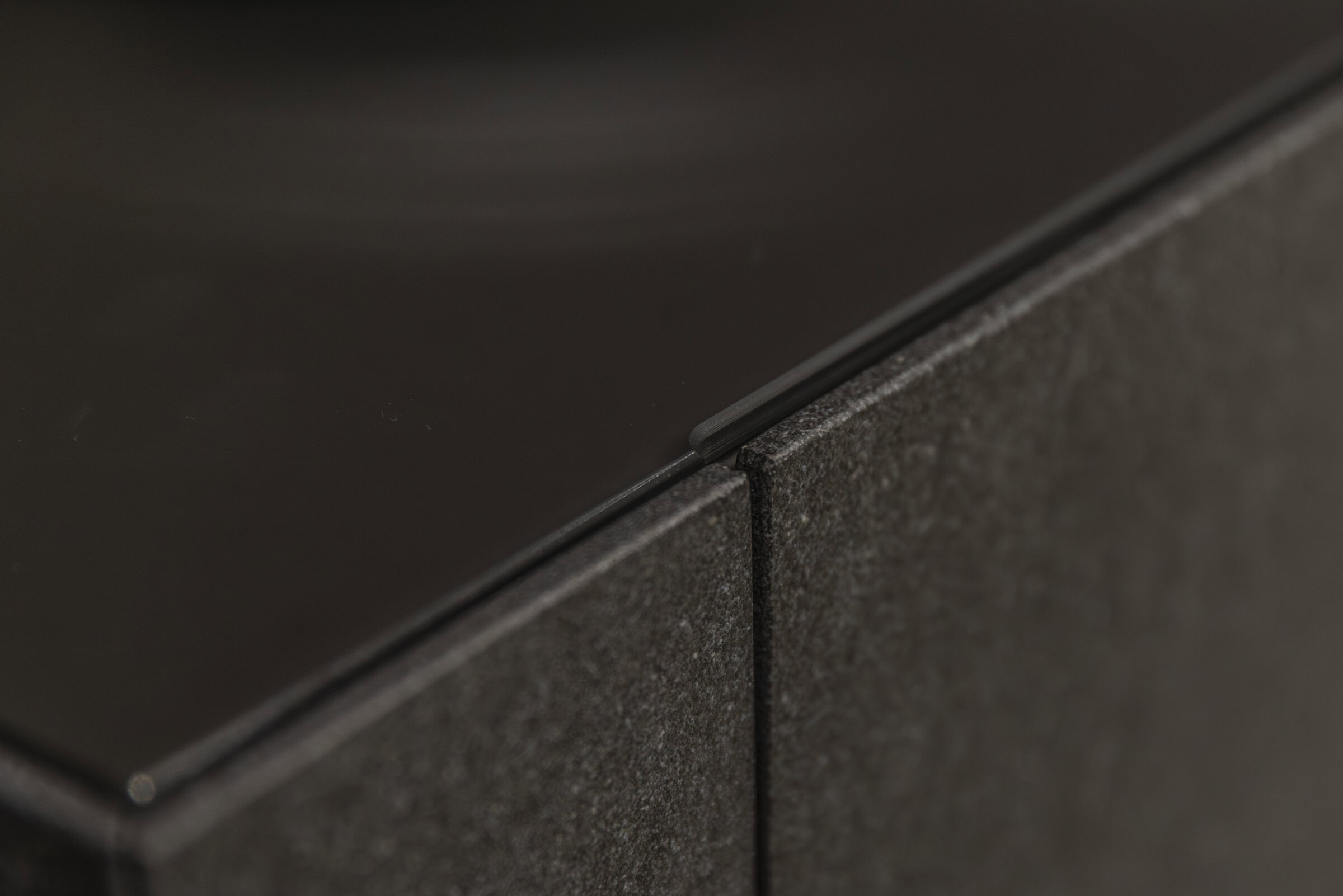 Sleek close-up view of dark wood and stone furniture joint, highlighting craftsmanship and modern design at Saloni Furniture.
