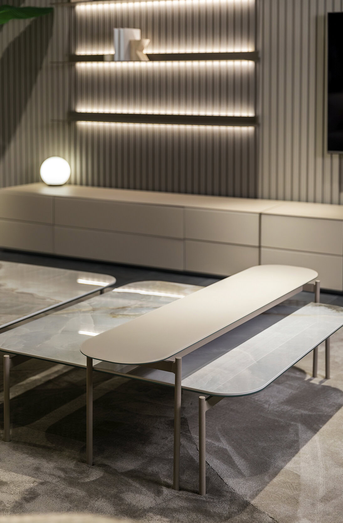 Contemporary living room with minimalist furniture, including a long white bench, glass coffee table, and ambient lighting on a textured wall.