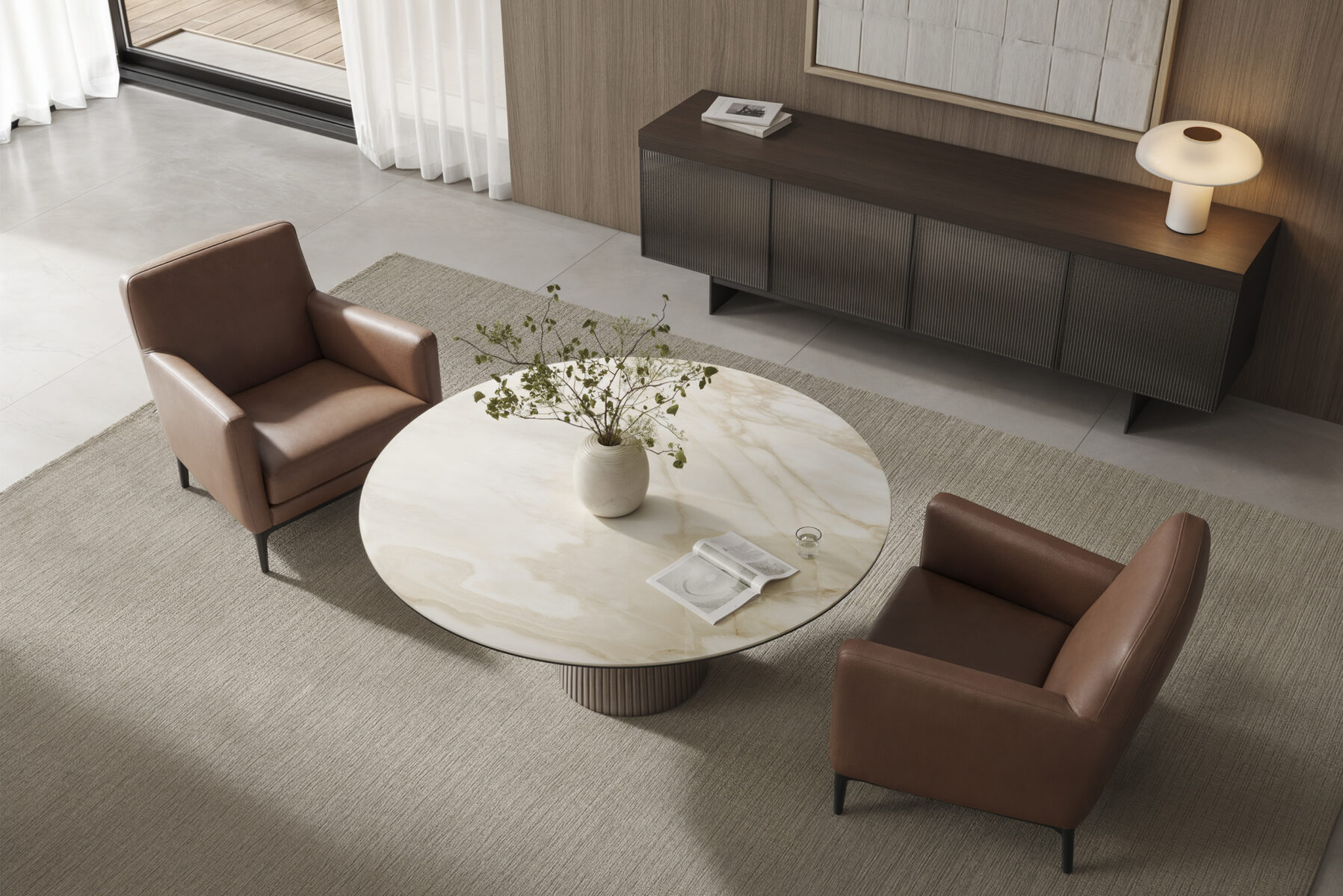 Elegant living room with modern leather armchairs, a round marble coffee table with a vase of green foliage, and contemporary wooden sideboard with a stylish table lamp.