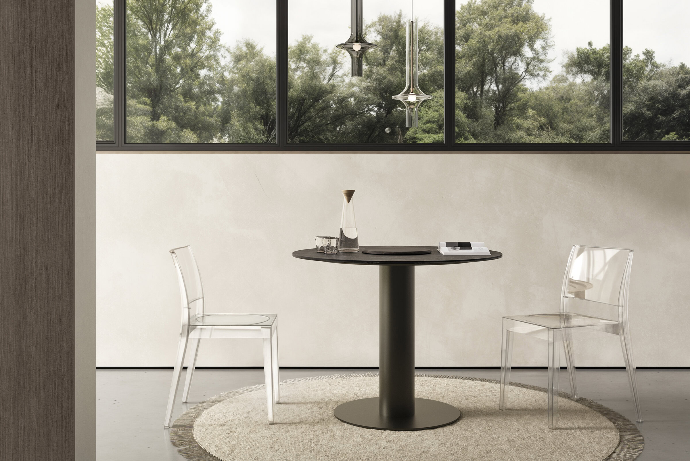 Modern round dining table with sleek black tabletop and sturdy base, paired with clear acrylic chairs, set against large windows with a lush green view, exemplifying contemporary minimalist furniture design.