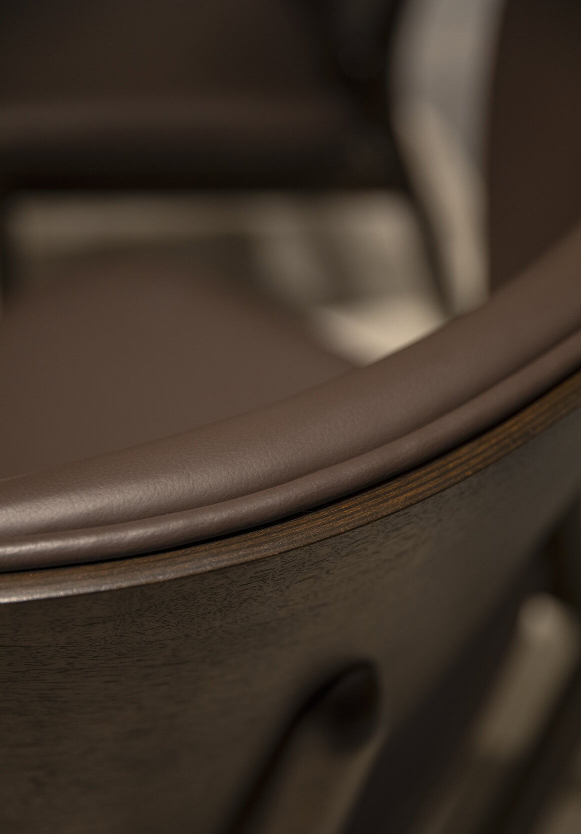 Elegant close-up of a brown leather upholstered chair with wooden accents, highlighting craftsmanship and premium furniture quality for living room or office decor.