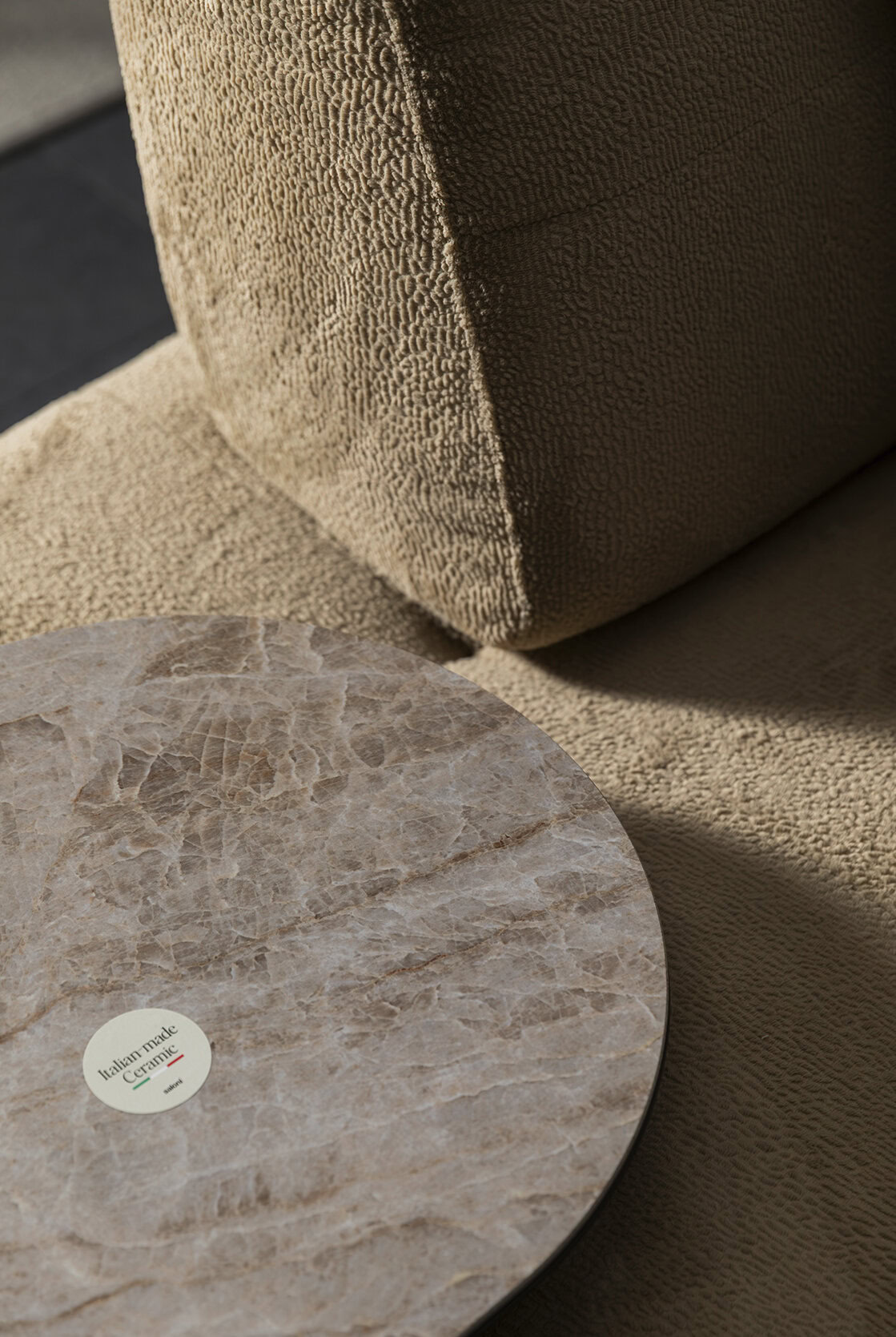 Close-up of a beige fabric sofa and a round marble coffee table in a stylish living room.